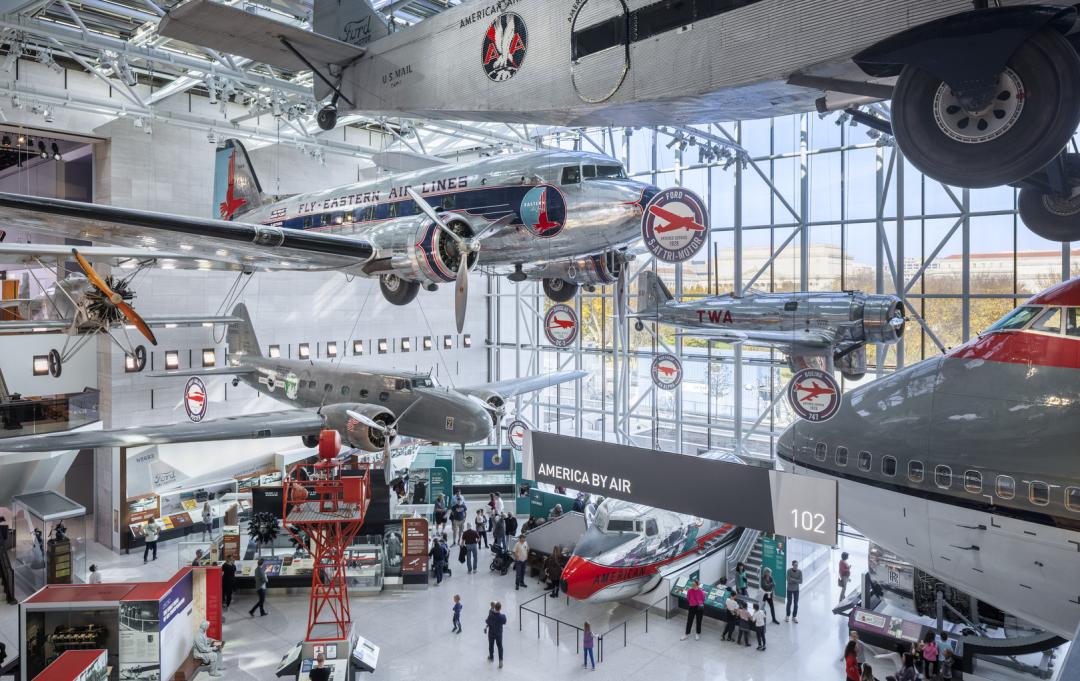 Silver airplanes are suspended in the air in an atrium of the Smithsonian's National Air and Space Museum